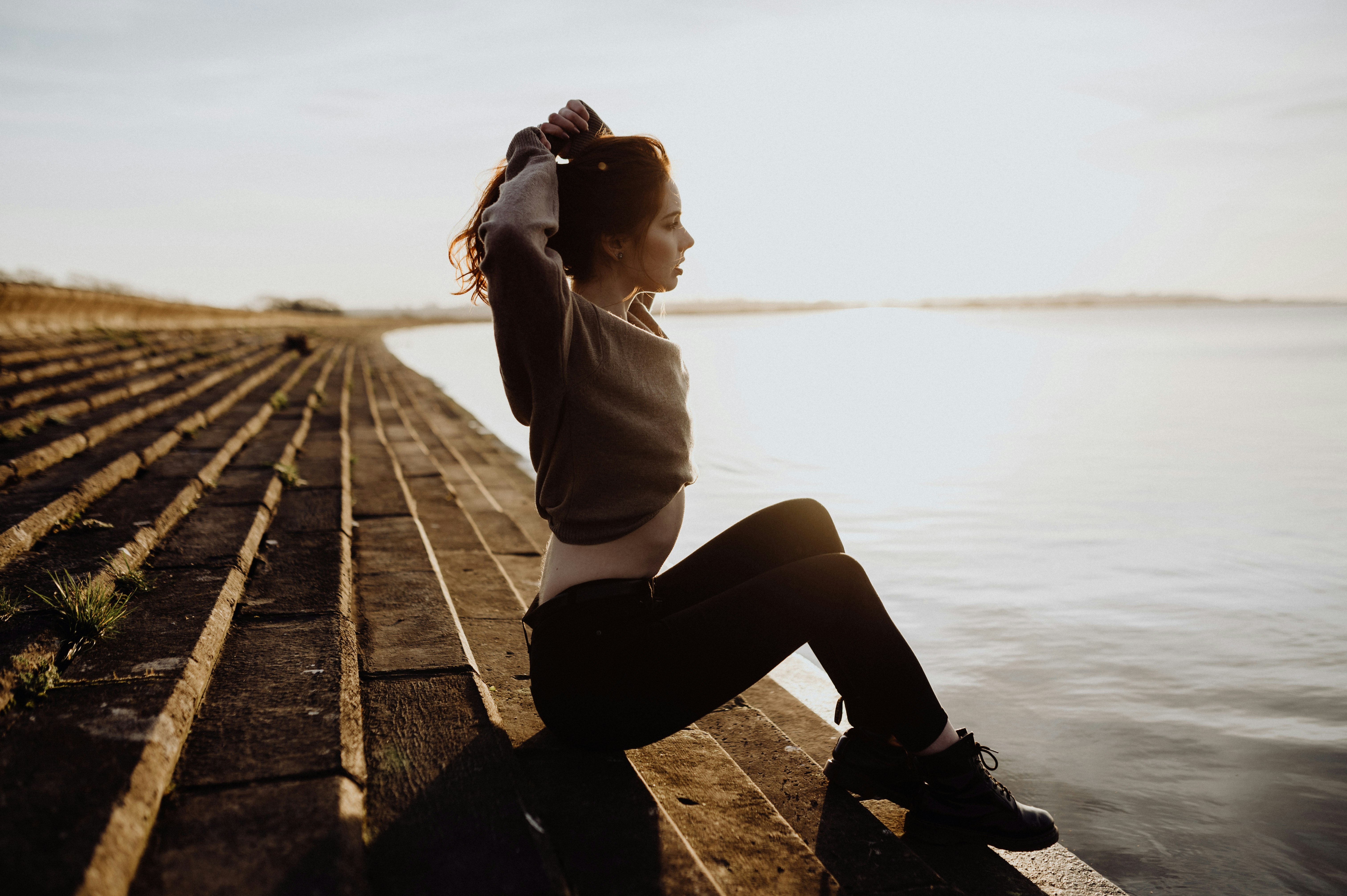 woman in white long sleeve shirt and black pants sitting on brown wooden dock during daytime